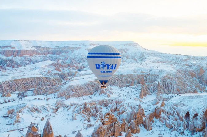A hot air balloon above a snowy valley of rock formations